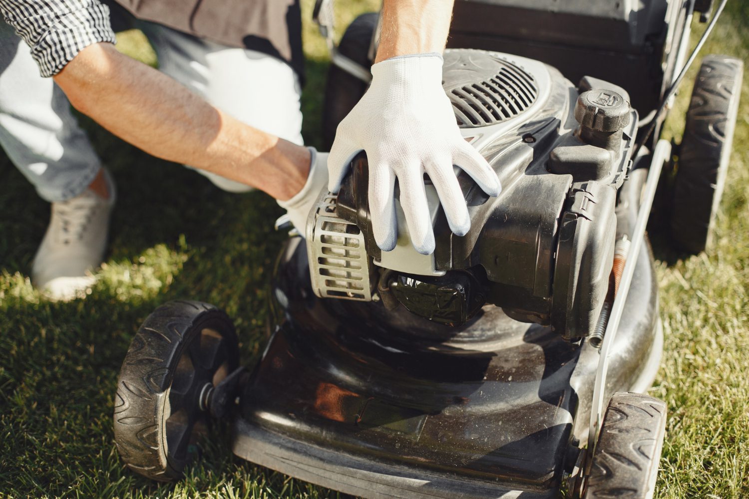 Man cutting grass with lawn mover in the back yard. Male in a black apron. Guy repairs.<br />
