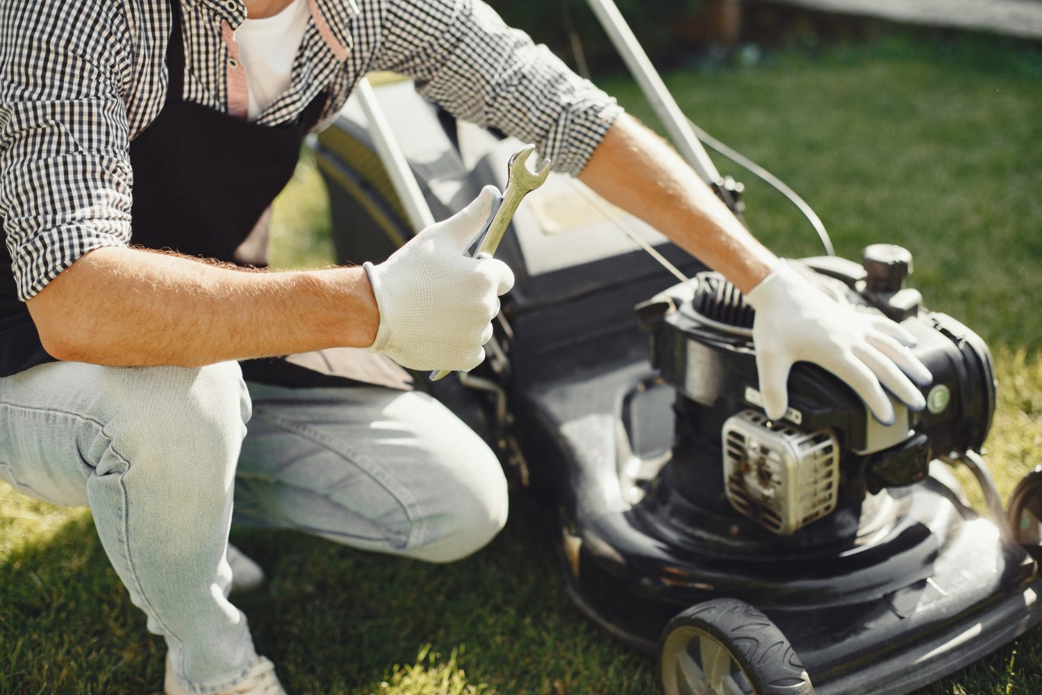 Man cutting grass with lawn mover in the back yard. Male in a black apron. Guy repairs.<br />
