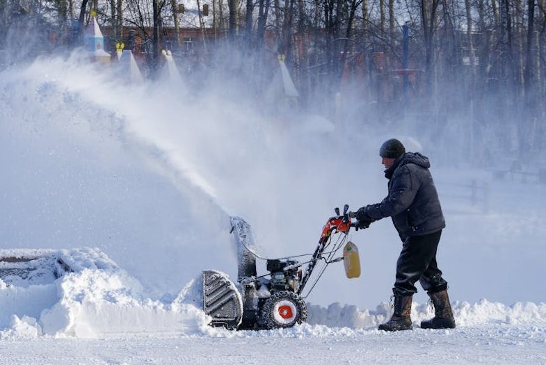Man in Green Jacket Using Snow Blower<br />